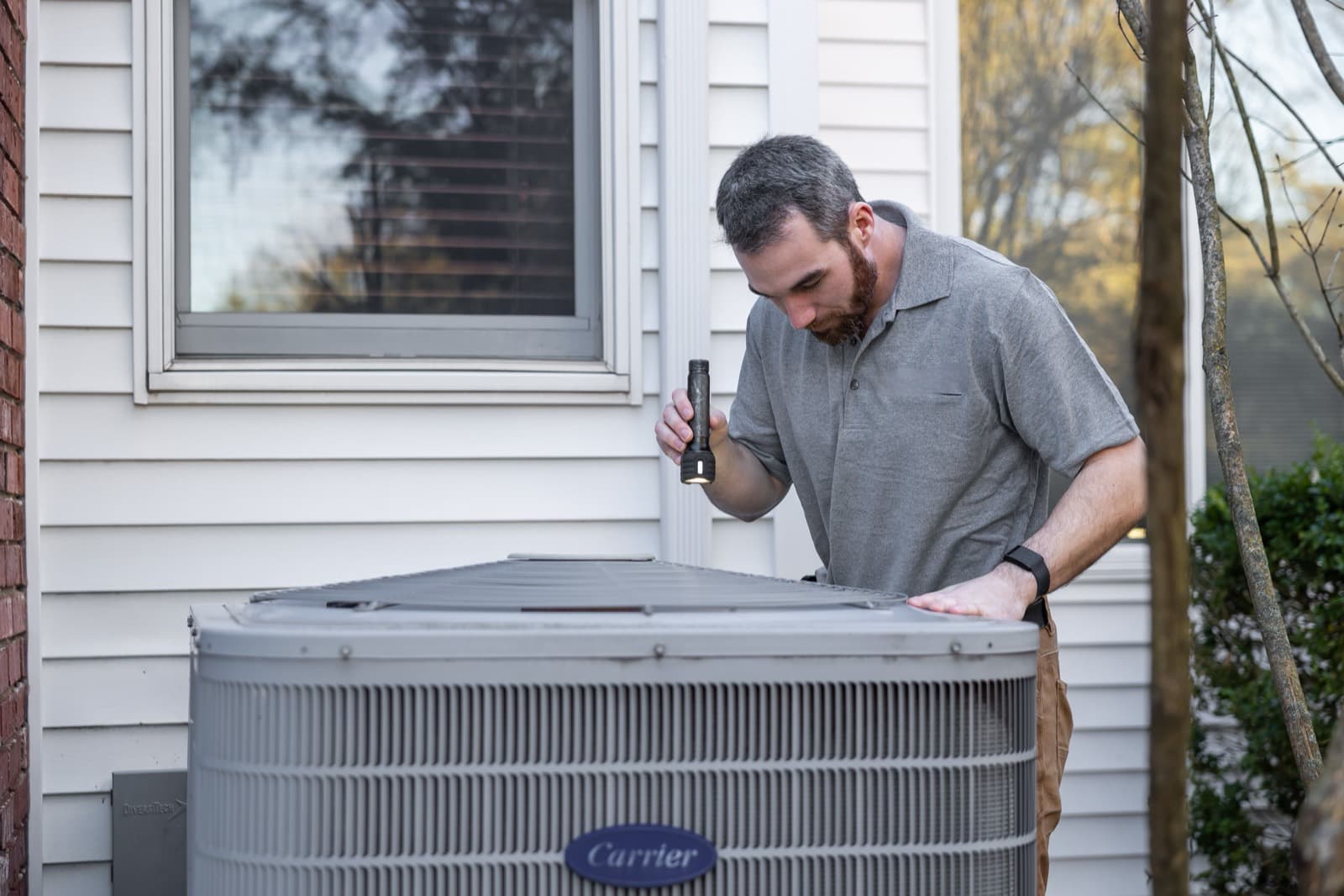 A technician inspecting an outdoor condenser unit with a flashlight