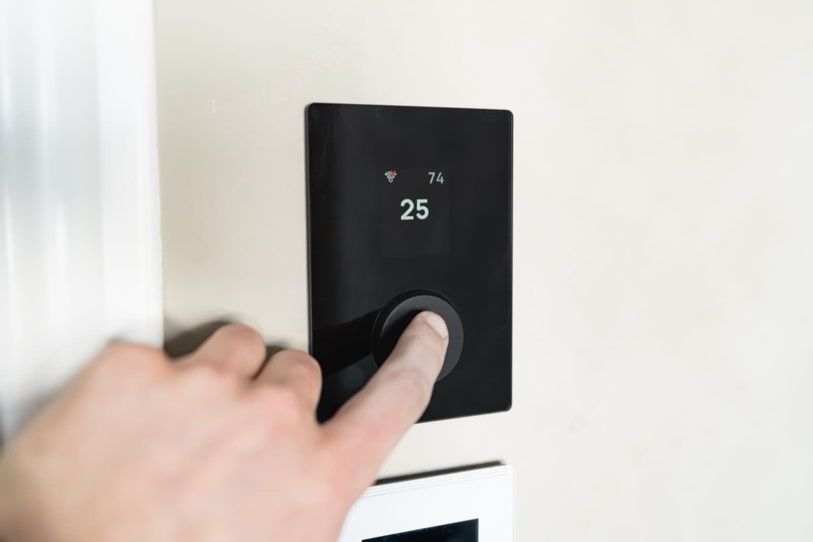 A hand adjusting a wall-mounted smart thermostat